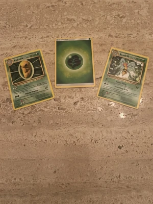 Pokémonkort: Kakuna, Beedrill & Energi - Tre Pokémonkort säljes: Kakuna, Beedrill och ett grönt Grass Energy-kort. Klassiska samlarkort i papp med färgglada illustrationer och text på engelska. Perfekt för dig som gillar Pokémon eller vill bygga din egen kortlek.