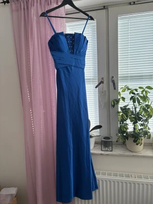 LAUTINEL Blå balklänning med pärldetaljer strl S/M (se bilder) - Elegant blå långklänning med smala axelband och v-ringad urringning dekorerad med pärlor och små stenar. Klänningen har veckade detaljer över bysten och midjan för en snygg siluett. Perfekt för speciella tillfällen. Storlek står som 3. Motsvarar ung S/M. Min dotter på bilden är 178 lång och har klänningen på sig. 