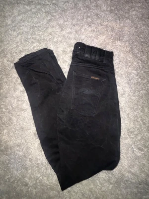  Nudie Jeans svarta - Säljer ett par svarta jeans från Nudie Jeans med klassisk femficksdesign och raka ben. Jeansen är nästan aldrig använda och är i bra skick