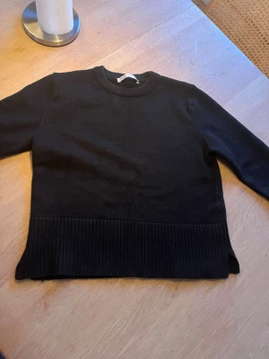 Svart stickad tröja från Zara - En svart stickad tröja från Zara med rund halsringning och bred ribbstickad kant nedtill. Tröjan har långa ärmar och en enkel, stilren design som passar till det mesta! Storlek L, säljer då den inte passar mig😍aldrig använd, endast testad🥰