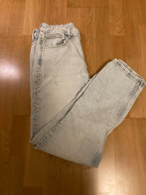 Ljusblå mom jeans i tvättad denim - Säljer ett par ljusblå mom jeans med hög midja och klassisk femficksmodell. Jeansen har en tvättad, nästan blekt look och raka ben. Perfekta för en avslappnad och trendig stil. Materialet är mjuk denim i bomull.