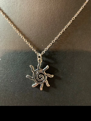 Silvrigt halsband med solhänge - Unikt halsband i silverfärgad metall med ett solformat hänge och spiral i mitten. Kedjan är tunn och smidig, perfekt för att ge en cool touch till din outfit. Märke ej angivet.