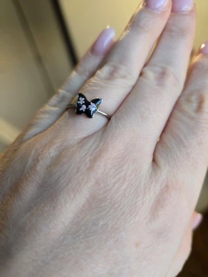 Söt ring med svart fjäril och blommor - Unik ring med en svart fjärilsformad detalj dekorerad med små rosa blommor. Rostfritt stål.