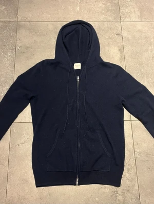 Mörkblå kashmir hoodie John Henric - Mörkblå hoodie i lyxig cashmere från John Henric. Dragkedja framtill, två fickor och justerbar huva med snören. Perfekt för dig som vill ha en stilren och bekväm hoodie i ett riktigt mjukt material.