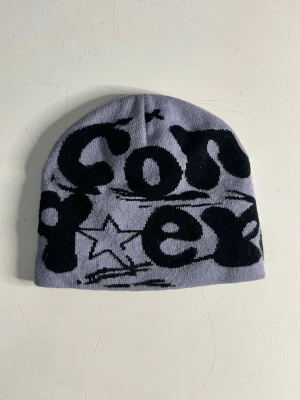 Ljuslila mössa med svart tryck - Säljer en ljuslila mössa med svart grafiskt tryck och stjärndetalj framtill. Mössan är mjuk och stretchig, perfekt för att hålla värmen och ge en cool streetstil. Passar dig som gillar unika accessoarer och vill sticka ut i mängden.