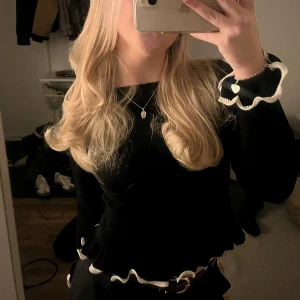 Svart långärmad topp med volang - Svart långärmad topp med vita volangdetaljer vid ärmslut och nederkant. Toppen är ifrån Gina och enbart använd enstaka gånger. Inga defekter och fint skick🌟