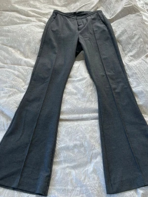 Grå kostymbyxor med utsvängda ben - Snygga grå kostymbyxor med pressveck och utsvängda ben. Byxorna har fickor i sidorna och en klassisk midja. Perfekta för en stilren look. Medel i midjan och st S✨