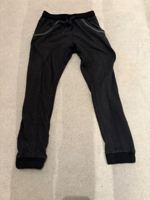 New Project Svarta mjukisbyxor 30 - Säljer ett par svarta mjukisbyxor med resår i midjan och dragsko. Byxorna har ribbade muddar vid bensluten, fickor fram och två bakfickor. Perfekta för chill eller träning. Materialet känns mjukt och stretchigt.