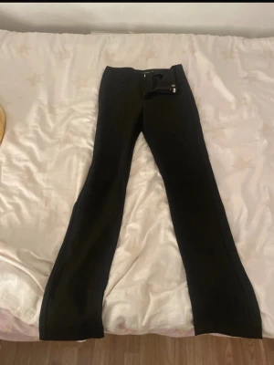 Svarta leggings med slits - Säljer ett par svarta leggings med slits vid bensluten. De har hög midja och en smickrande, tight passform. Materialet är stretchigt och bekvämt, perfekt för en trendig och avslappnad look. Inga synliga loggor eller märken.