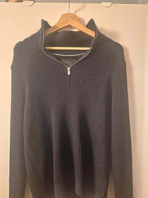 Mörkblå stickad tröja Jack & Jones - Snygg mörkblå stickad tröja från Jack & Jones med ribbad struktur och halv dragkedja framtill. Tröjan har hög krage och långa ärmar, perfekt för lager på lager. Klassisk och stilren design som passar till det mesta.