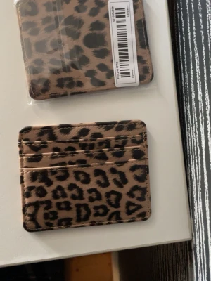 Leopardmönstrad kortfodral - Säljer ett snyggt kortfodral med leopardmönster i beige och svart. Fodralet har flera fack för kort och är tillverkat i ett slätt syntetmaterial. Perfekt för dig som vill ha en trendig och praktisk plånbok med cool design. Du får hem den oöppnade😊