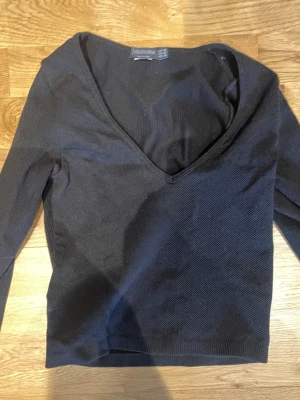 Svart v-ringad topp från Stradivarius💕 - Snygg svart topp från Stradivarius med djup v-ringning och lång ärm. Modellen är croppad och har en tight passform som framhäver siluetten.💕