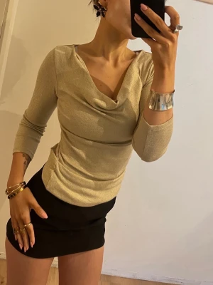 Vintage Glittrig guldfärgad topp med drapering✨ - Snygg vintage guldfärgad topp med glittrig finish och draperad urringning. Modellen har trekvartsärm och figurnära passform. Perfekt för dig som vill sticka ut lite. 