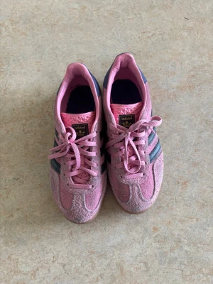 Adidas rosa sneakers med blå ränder - Säljer ett par snygga Adidas sneakers i rosa mocka med klassiska blå ränder på sidorna och gummisula. Säljer då de är lite för små för mig så inte fått mycket användning av de:( så fina och roliga till vår och sommar🩷🩷🩷 jättebra skick förutom lite missfärgade baktill. Skulle säga att de passar nån som har upp till storlek 37 då de är lite större