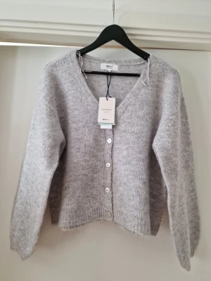 Ljusgrå stickad kofta XS - OBS kolla min annons med samma produkt och fri frakt. Mysig ljusgrå stickad kofta från Gina Tricot med v-ringning och fyra vita knappar framtill. Storlek XS. Koftan har lång ärm och är gjord i en mjuk, fluffig ullblandning som känns riktigt skön. Perfekt att slänga över en t-shirt eller topp för extra värme.