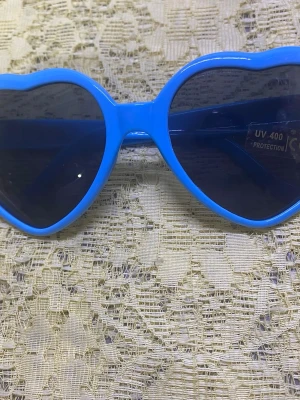 Hjärtformade solglasögon  - Två par solglasögon med hjärtformade bågar, ett par i klarblått och ett i klargult. Båda har mörka linser med UV400-skydd. Perfekta för att sticka ut och ge en lekfull touch till din stil. Tillverkade i plast.  69kr/st 