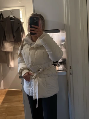 Krämvit pufferjacka med knytskärp - Oanvänd jacka med knytdetalj. Har liknande så denna har tyvärr aldrig kommit till användning. 