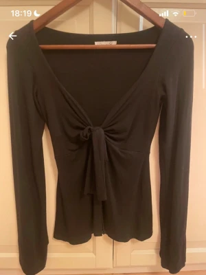 Design by si svart tröja  - Trendig svart omlottopp med lång ärm och snygg knytning framtill. Djup v-ringning och figurnära passform som framhäver siluetten. Perfekt att styla med jeans eller kjol för en cool look. Använd få gånger! Storlek Xs/S