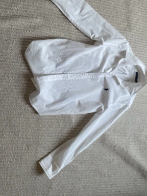 Vit skjorta från Ralph Lauren - Klassisk vit skjorta från Ralph Lauren med lång ärm och knappar framtill. Skjortan har en liten broderad logga på bröstet och är tillverkad i bomull. Perfekt till en clean och stilren look.