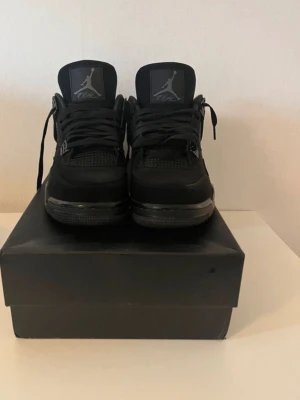 Svarta Air Jordan 4 Retro sneakers - Säljer ett par helsvarta Air Jordan 4 Retro sneakers med klassisk Jumpman-logga på plösen. Skorna har meshdetaljer, grova snören och robust sula. Perfekta för dig som gillar streetwear och vill ha en ikonisk look.