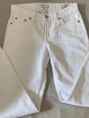 Vita raka jeans från ZARA - Snygga vita jeans från ZARA med rak passform och klassisk femficksdesign. Jeansen har silverfärgade nitar och knapp, samt bälteshällor i midjan. Perfekta för en fräsch och stilren look.