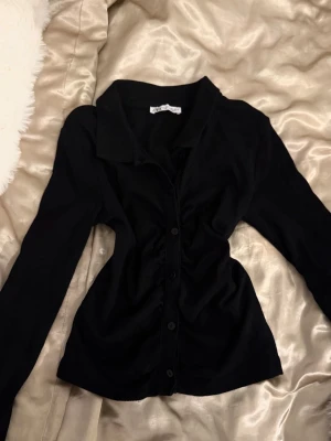 Svart långärmad skjorta från Zara - Svart skjorta från Zara med lång ärm och klassisk krage. Skjortan har knappar framtill och är figurnära i modellen. Perfekt för dig som gillar en stilren och enkel look.