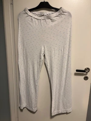 Vita pyjamasbyxor med småblått mönster - Mysiga vita pyjamasbyxor med smått blått mönster över hela tyget. Byxorna har resår i midjan och är tillverkade i ett mjukt och tunt material som känns skönt mot huden. Perfekta för slappa dagar hemma eller när du vill ha det extra bekvämt.