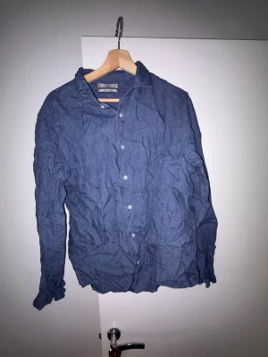 Blå linneskjorta från MNG - Säljer en blå skjorta från MNG i regular fit, tillverkad i linne. Skjortan har klassisk krage, knappar framtill och långa ärmar. Perfekt för dig som gillar en avslappnad och stilren look.