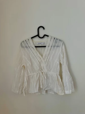 Vit blus  - Söt vit omlottblus från NA-KD med broderade detaljer och spets längs v-ringningen. Blusen har knytband i midjan 