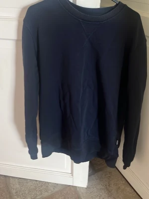 Mörkblå basic sweatshirt - En stilren mörkblå sweatshirt med rund halsringning och ribbade muddar vid ärmslut och nederkant. Tröjan är enkel och passar perfekt till jeans eller joggers och klassisk passform. Slutat använda den