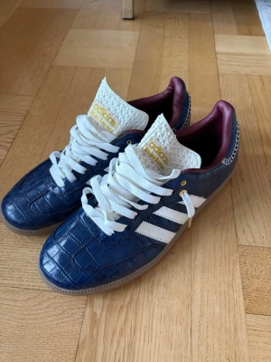 Adidas X Wales bonner skor - Snygga blå sneakers från Adidas med krokodilmönstrad yta, vita klassiska stripes och vit plös med gul Adidas-logga. Skorna har vinröd insida och vita skosnören. Perfekt för dig som vill sticka ut med en unik stil. INTRESSE KOLL