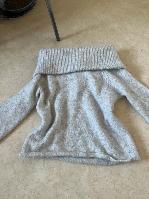 Ljusgrå off shoulder stickad tröja - Mysig ljusgrå stickad tröja med bred, nedvikt krage som kan bäras off shoulder. Tröjan är använd en gång (fel storlek) men den är jätte fin. Om man vill ha fler bilder på plagget (på eller andra vinklar) är det bara att säga till så fixar jag det