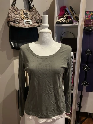 Peak Performance långärmad topp - Stilren och bekväm långärmad topp från Peak Performance i en snygg grön/oliv färg. Mjukt och stretchigt material som sitter fint och är skönt att bära hela dagen. Diskret Peak Performance-tryck framtill ger en sportig och minimalistisk look. Perfekt både till vardag, fritid eller en avslappnad outfit.