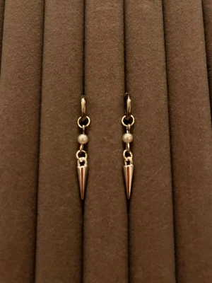 Silvriga örhängen med pärldetalj - Säljer ett par stilrena silvriga örhängen med små vita pärlor och spetsiga hängande detaljer. Örhängena har en minimalistisk design och passar perfekt för dig som gillar en edgy men enkel look. Materialet ser ut att vara metall med pärldetalj.