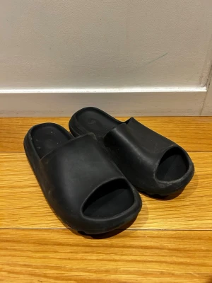 Slippers *42* - Säljer ett par svarta tofflor med chunky sula och öppen tå. Tillverkade i mjukt gummi för maximal komfort. Snygg minimalistisk design med räfflad undersida för extra grepp. Perfekta för att glida runt hemma eller på stan.