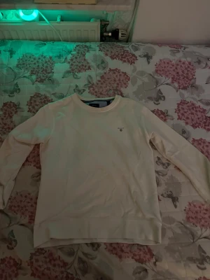 Vit sweatshirt från GANT strl 170cm 15 years - Snygg vit sweatshirt från GANT med rund halsringning och diskret logga på bröstet. Tröjan har långa ärmar och ribbade muddar vid ärmslut och nederkant. Perfekt för en clean och klassisk stil.