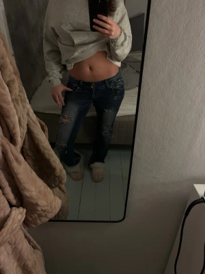 Mörkblå slitna jeans med hål - Säljer ett par mörkblå jeans med låg midja och slitningar samt hål på båda benen. Jeansen är bootcut . Perfekta för en avslappnad och trendig look.