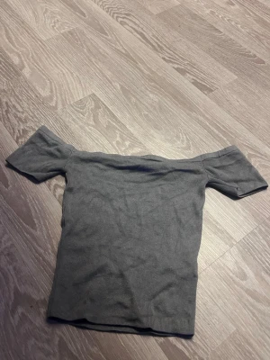 Grå offshoulder topp från H&M Divided - Säljer en grå ribbad offshoulder topp från H&M Divided i storlek XS. Toppen har en tight passform och ärmlös design med korta ärmar som sitter snyggt över axlarna. Perfekt för dig som gillar en enkel men trendig stil.