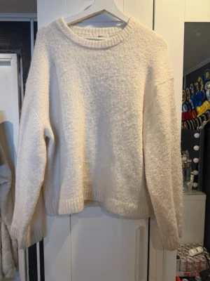 Krämvit stickad tröja - Mysig krämvit stickad tröja med rund halsringning och avslappnad passform. Tröjan har långa ärmar och ribbstickade muddar vid ärmslut och nederkant. Perfekt för lager-på-lager och enkel att matcha med jeans eller kjol.