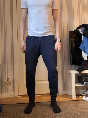 Mörkblå mjukisbyxor med dragsko - Säljer ett par mörkblå mjukisbyxor med dragsko i midjan och ribbade muddar vid bensluten. Byxorna har fickor på sidorna och en avslappnad passform. Perfekta för chill dagar hemma eller när du vill vara bekväm.