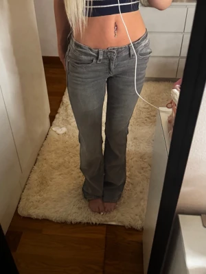 Grå lågmidjade bootcut jeans med fickdetaljer - Snygga grå bootcut jeans med låg midja och coola fickdetaljer bak. Jeansen har klassisk femficksdesign och är i ett mjukt denimtyg som sitter skönt. Perfekta för en trendig och avslappnad look.