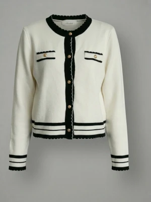 Vit och svart kofta med guldknappar - Stilren vit kofta med svarta detaljer och dekorativa guldknappar. Koftan har rund halsringning, två fejkade bröstfickor och svarta ränder vid ärmslut och nederkant. Materialet är mjukt och koftan har en klassisk, lite kortare passform.