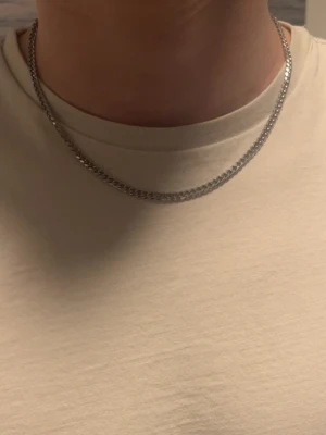 Kedjehalsband i silverfärg - Snyggt halsband med klassisk kedjedesign i silverfärgad metall. Materialet är rostfritt stål. I lager finns flertal storlekar. 45cm 4mm, 50cm 4mm, 45cm 6mm, 50cm 6mm. Köp produkten och skriv vilken du vill ha.