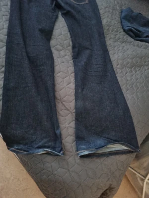 Mörkblå bootcut jeans - Säljer ett par mörkblå bootcut jeans med klassiska bakfickor och kontrastsömmar. Jeansen har en snygg utsvängd passform och är tillverkade i denim. Perfekta för dig som gillar en retrostil och vill ha ett par jeans som sticker ut. Storlek 42 använd fåtal gånger mörkblå 