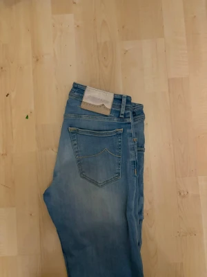 Ljusblå raka jeans från Jacob Cohën - Säljer ett par ljusblå jeans från Jacob Cohën med raka ben och klassisk femficksdesign. Jeansen har snygga slitningar och en patch i mocka bak på linningen. Tillverkade i mjuk denim med en avslappnad passform.