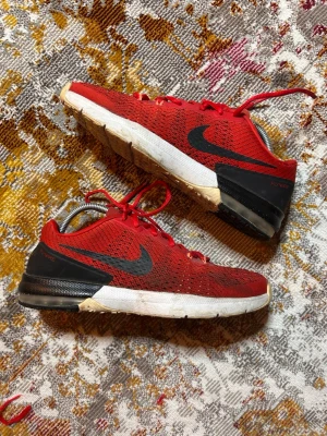 Röda Nike sneakers med svart swoosh - Snygga röda Nike sneakers med svart swoosh på sidan och svart hälparti. Ovandelen är i mesh för bra andningsförmåga och sulan är vit med beige detaljer. Skorna har röda skosnören och märkningen Flywire på hälen.