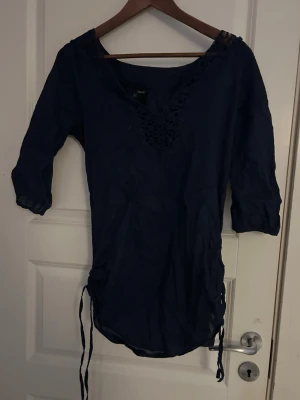 Mörkblå blus - Säljer en mörkblå blus med spets vid kragen och är justeringbar längst ner, jätte skön och luftig, perfekt att ha bikini under och spendera en dag på stranden med den 