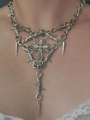 Silvrigt halsband med kors och taggar - Unikt halsband i silverfärgad metall med barbed wire-design, spetsiga taggar och ett stort kors i mitten. Kedjan har flera detaljer som ger en edgy och alternativ look. Perfekt för dig som gillar statement-smycken och vill sticka ut.