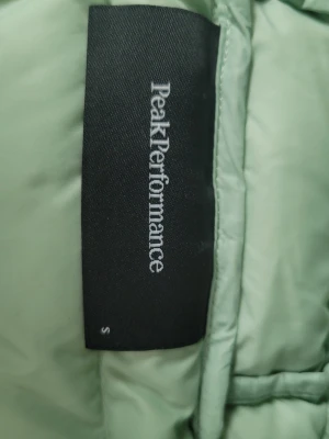 Ljusgrön dunjacka från Peak Performance  - Snygg ljusgrön dunjacka från Peak Performance i storlek S. Västen har quiltad design, hög krage och är tillverkad i ett lätt, vadderat material som håller värmen. Perfekt för lager-på-lager och ger en sportig vibe till din outfit.
