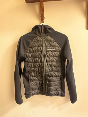 Svart vindjacka från Peak Performance - svart vindjacka från Peak Performance med quiltad front och rygg samt släta ärmar. Jackan har hel dragkedja, hög krage och två sidofickor med dragkedja.